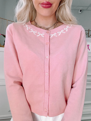 Pink button cardigan with embroidered bow detail.
