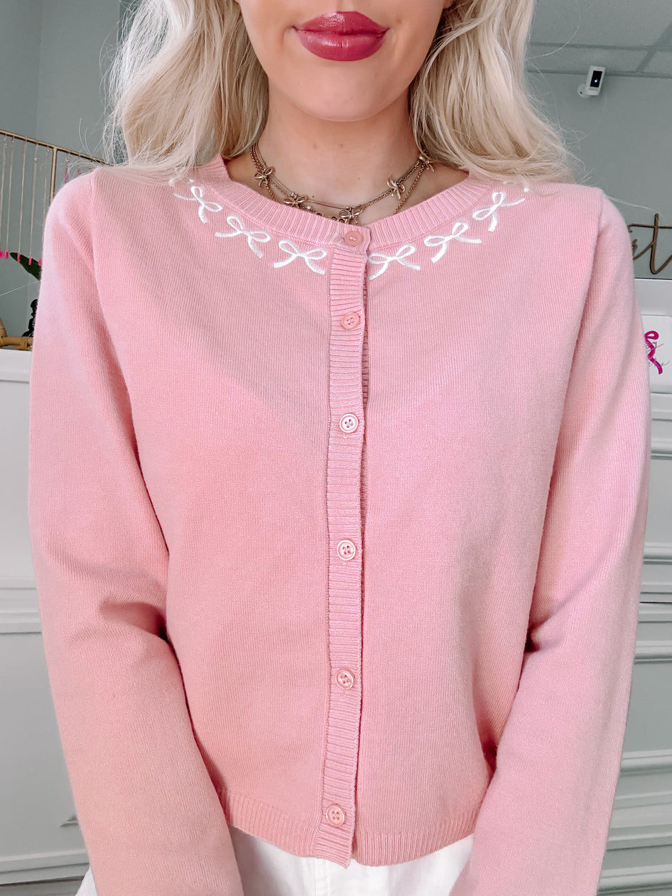 Pink button cardigan with embroidered bow detail.
