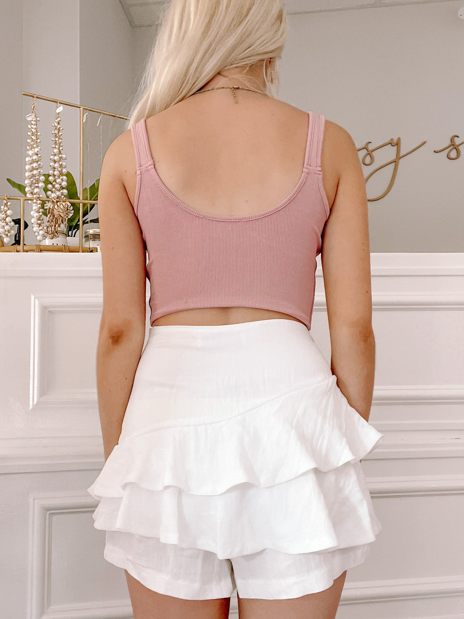 White ruffle-layered shorts; back view, styled with a mauve ribbed tank.
