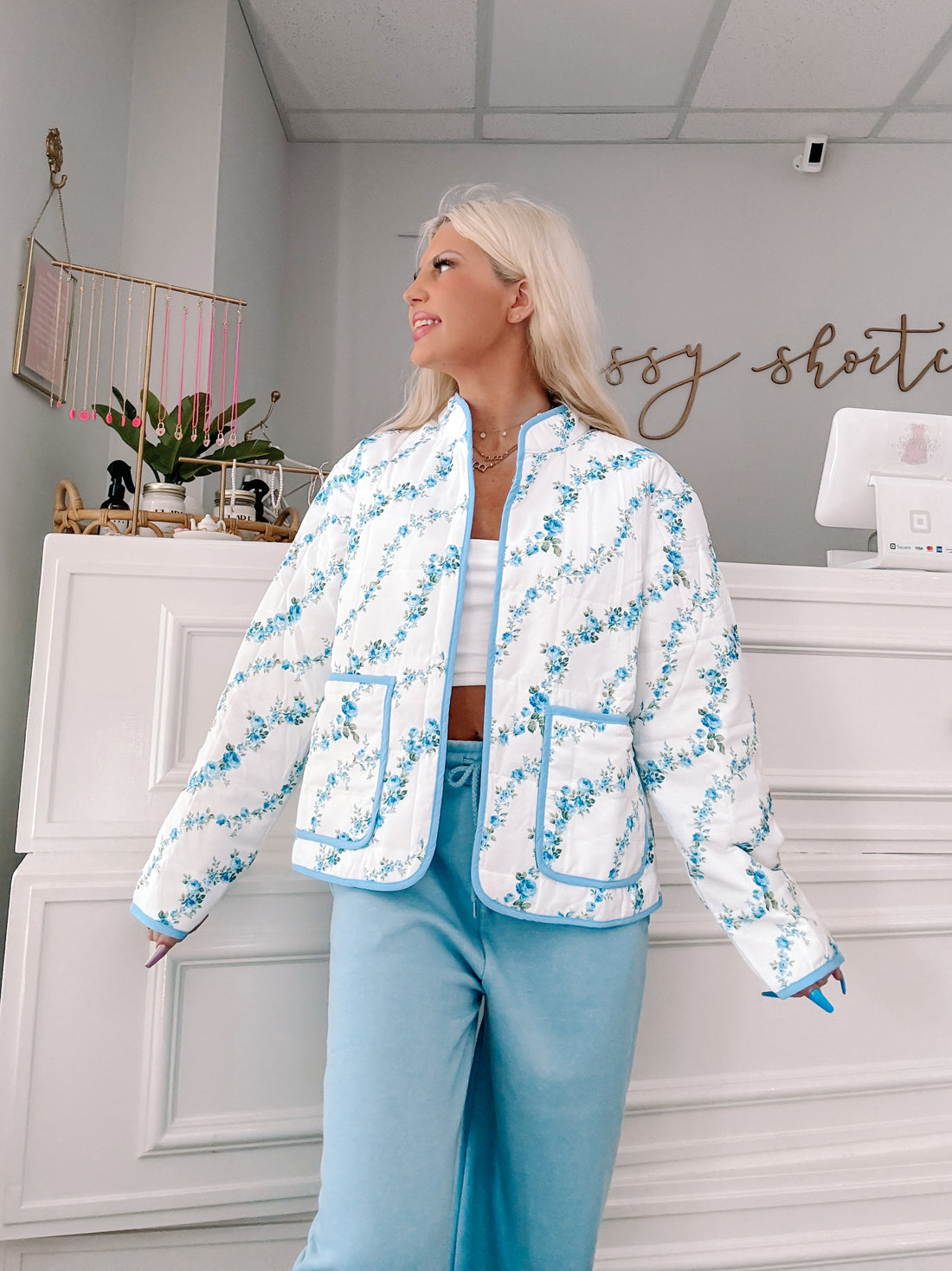 Blue floral quilted jacket with light blue trim, modeled against a white background.
