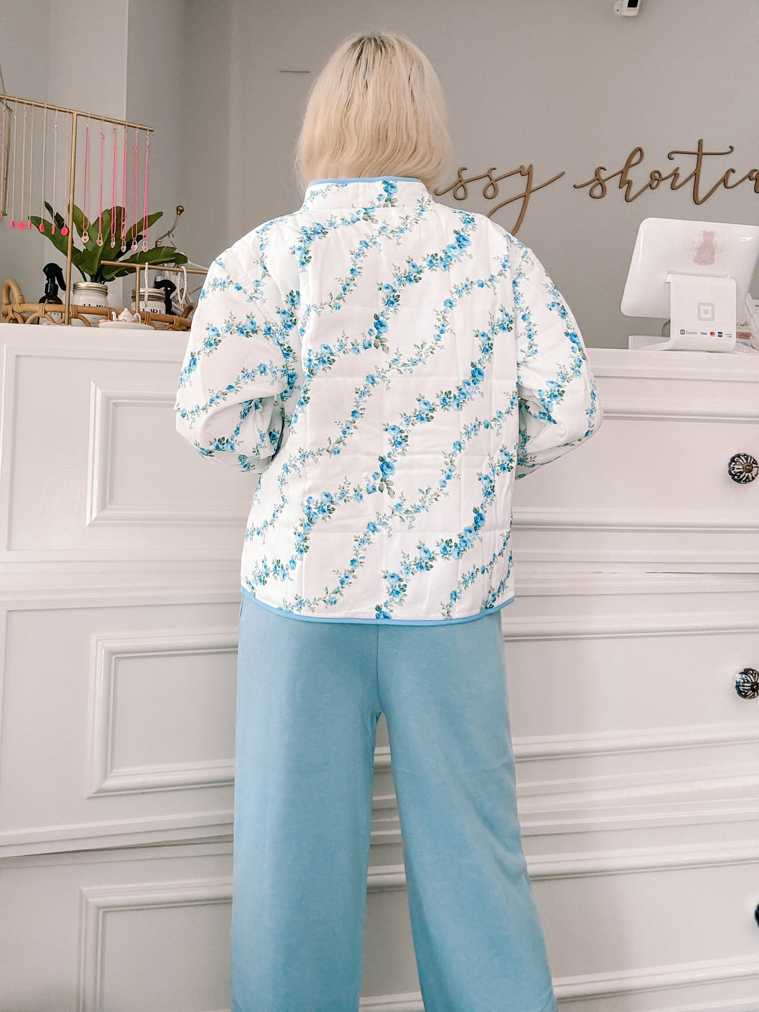 Blue floral quilted jacket, rear view, light blue pants.
