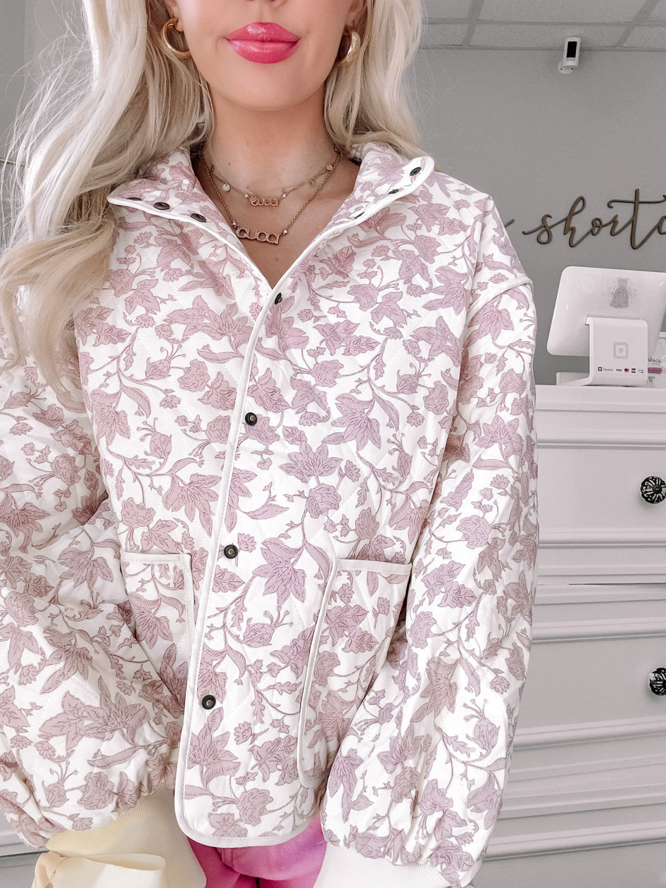 White quilted jacket with a delicate mauve floral print, shown on a model.

