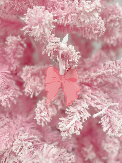 Pink bow ornament hanging on a flocked pink Christmas tree.
