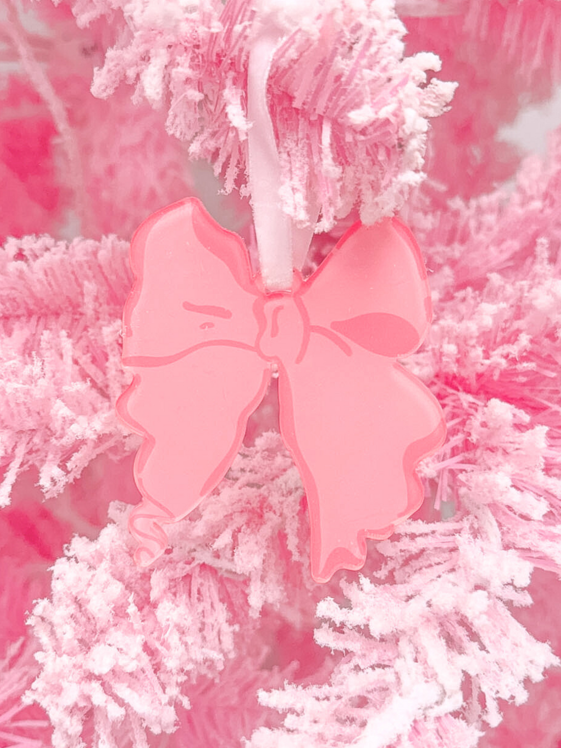 Pink resin bow ornament hanging on a fluffy pink Christmas tree.

