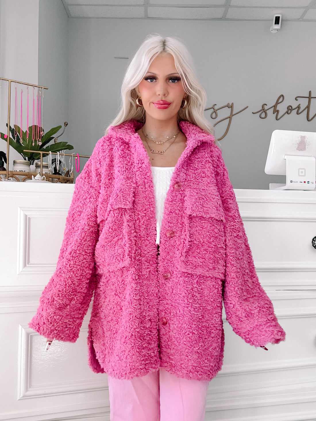 Fuzzy pink button-up jacket, styled with matching pants, shown on a model in a boutique setting.
