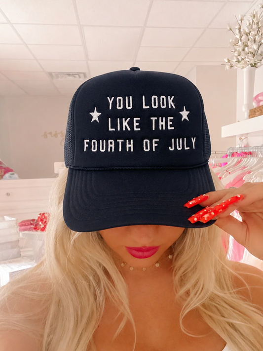 Navy You Look Like the Fourth of July trucker hat from Sassy Shortcake with white embroidered lettering and star accents, styled on a blonde model 