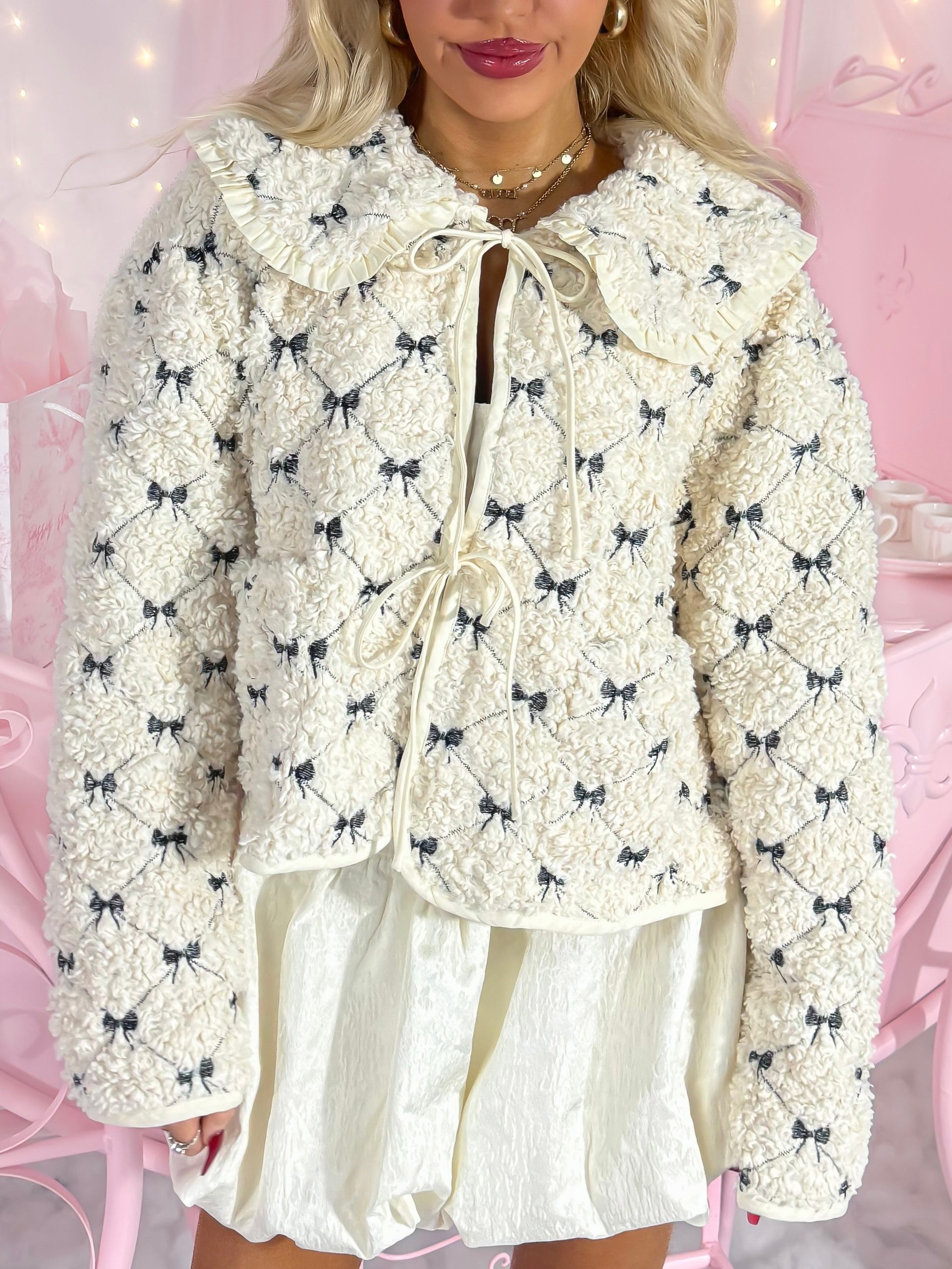 Cream Frosted Bow Jacket with black bow detail, ruffle collar, and tie closure.
