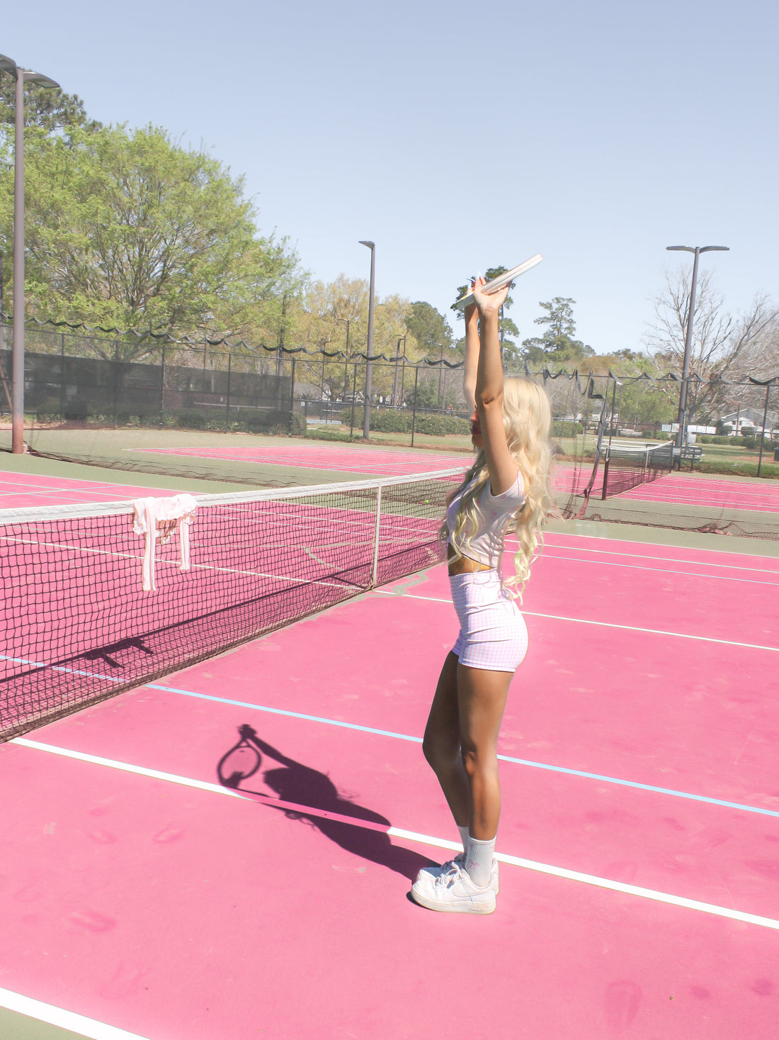 Woman in pink gingham shorts on a pink tennis court, holding a tennis racket overhead.
