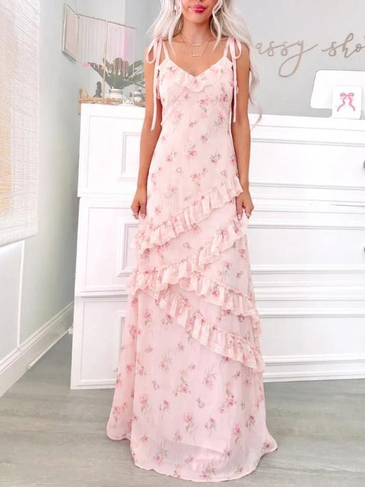 A blonde woman wearing a floor-length blush pink floral maxi dress with asymmetrical ruffles and tie-shoulder straps  Garden Romance Floral Maxi from Sassy Shortcake