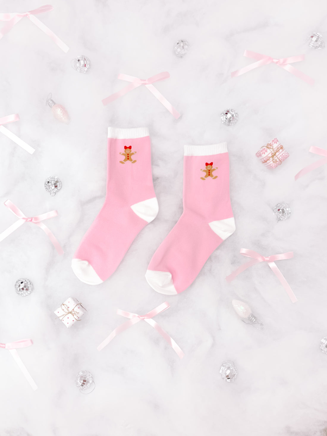 Pink socks with gingerbread man design, arranged on marble with festive decor.
