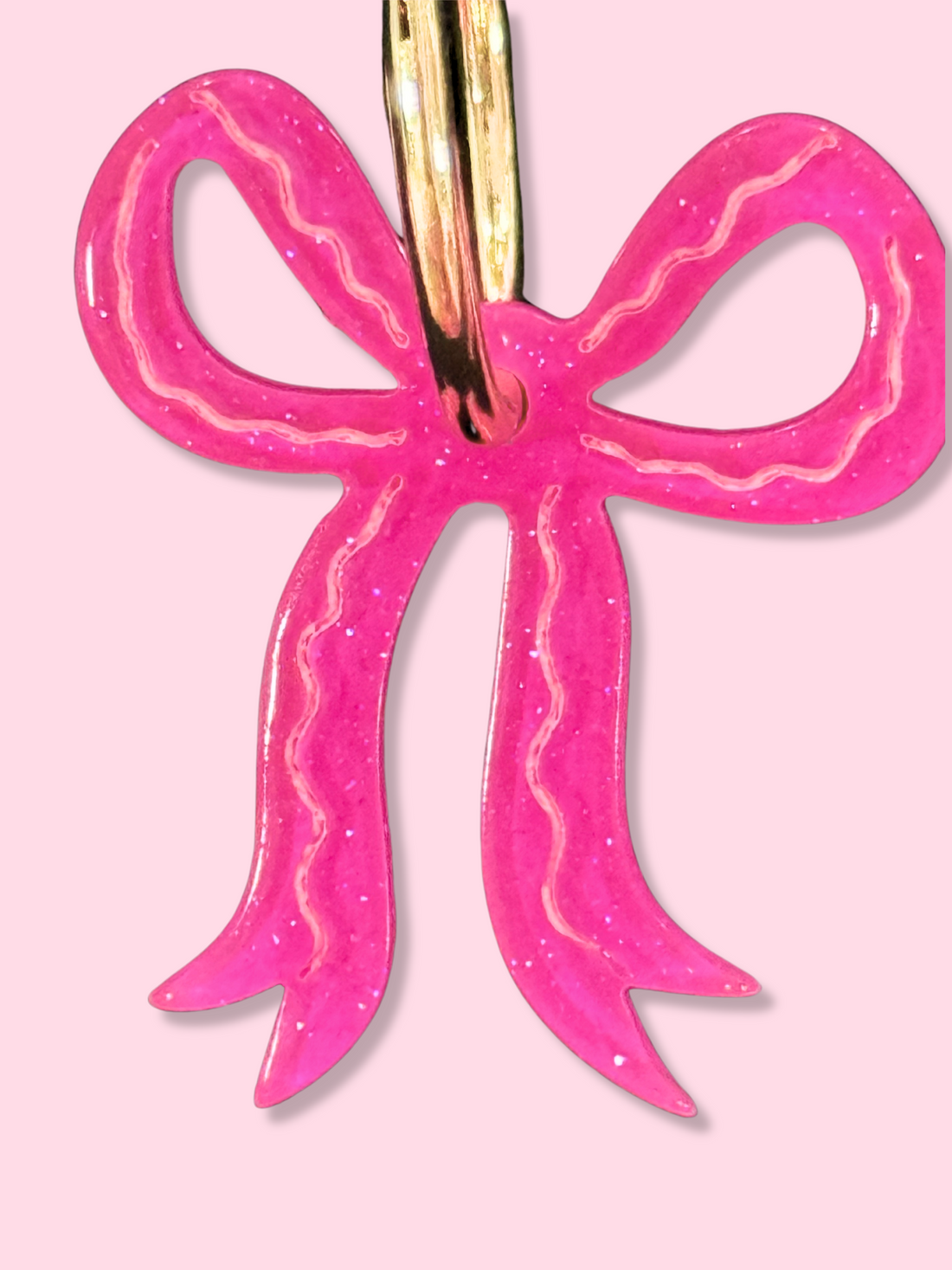 Pink glitter bow earrings with gold hoops; close-up view.
