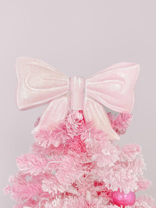 Pink glitter bow tree topper adorns a flocked pink artificial Christmas tree.
