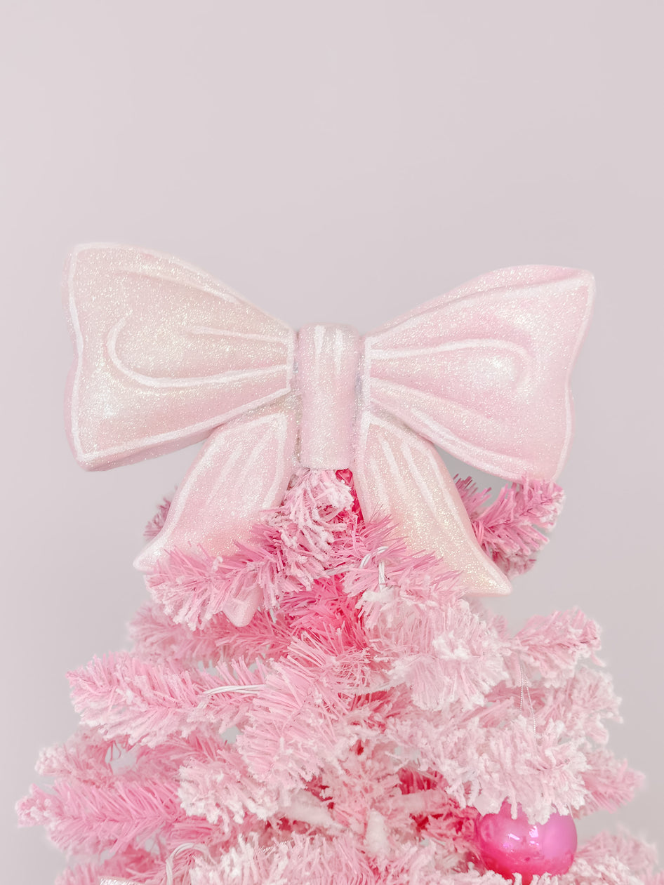 Pink glitter bow tree topper adorns a flocked pink artificial Christmas tree.
