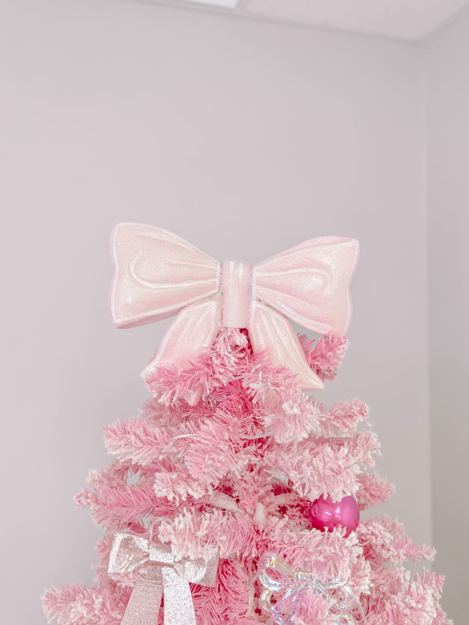 Pink glitter bow tree topper on a flocked pink Christmas tree.
