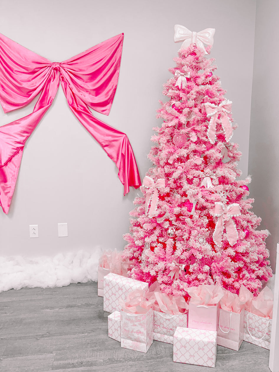 Pink Christmas tree decorated with bows and ornaments, presents at the base, and a large pink bow on the wall.
