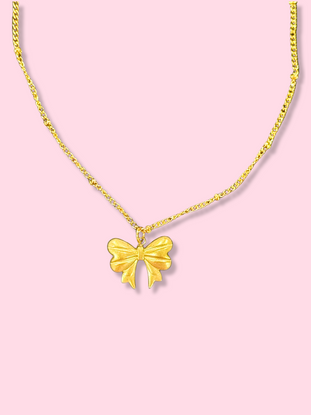 Gold bow pendant necklace on pink background.

