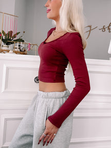 Burgundy long-sleeve fitted top with lace trim, modeled against a white wall.
