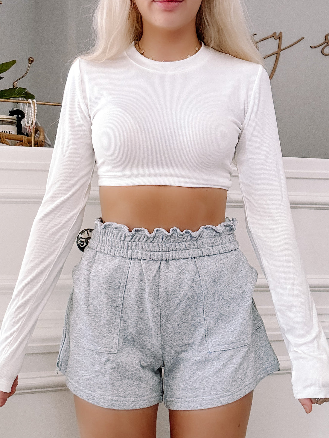 Grey zip-front shorts with a ruffled waistband, styled with a white ribbed long-sleeve crop top.
