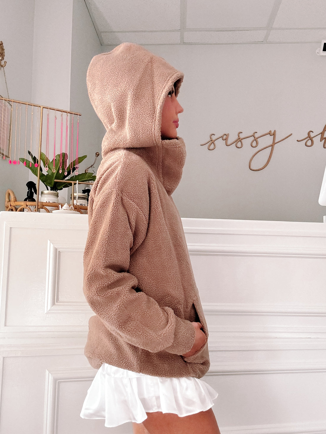 Cozy taupe teddy pullover with a drawstring hood, shown in profile against a white wall.
