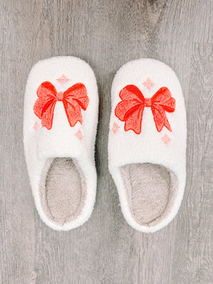 White fuzzy slippers with coral bows, perfect for cozy holiday relaxation.
