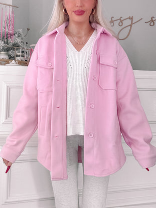 Pink shacket styled over a cream sweater, shown on a model against a white wall.
