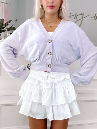Lavender button-up cardigan paired with a white tiered mini skirt.
