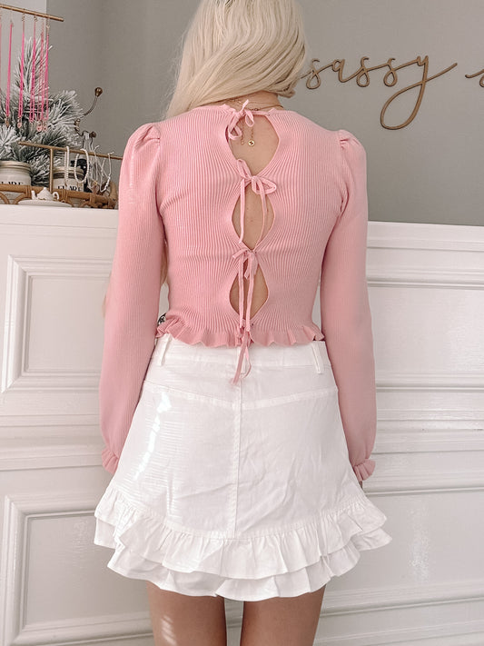 Pink ribbed knit top with open back and tie detail, styled with white ruffle shorts.