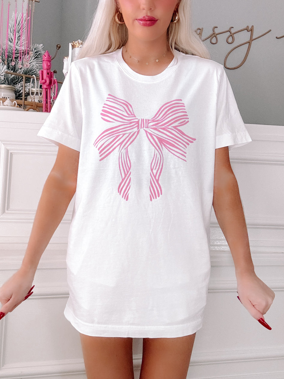 White oversized tee featuring a pink striped bow graphic.
