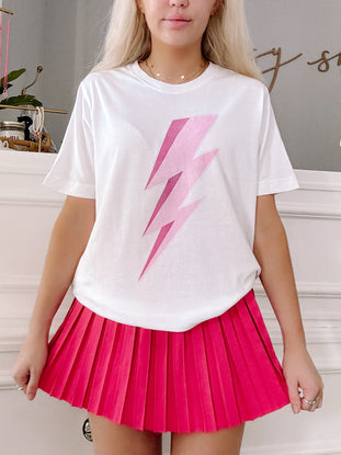 White tee shirt featuring a pink lightning bolt graphic, modeled with a hot pink pleated skirt.
