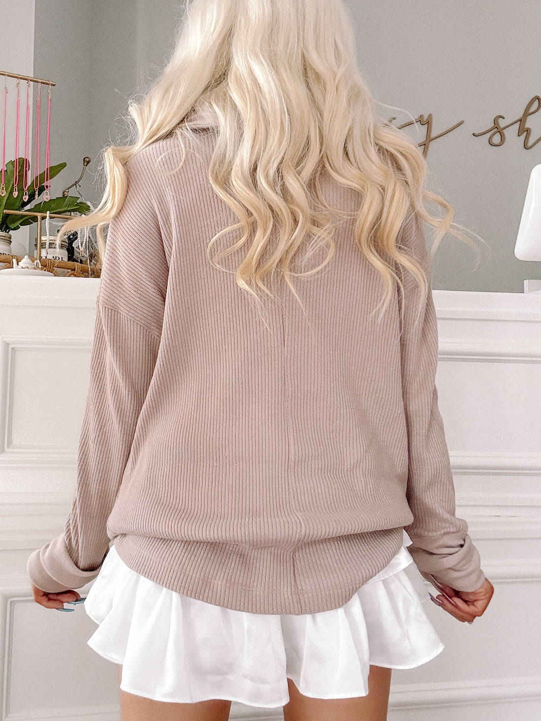 Taupe ribbed knit pullover with long sleeves, paired with a white ruffled mini skirt.
