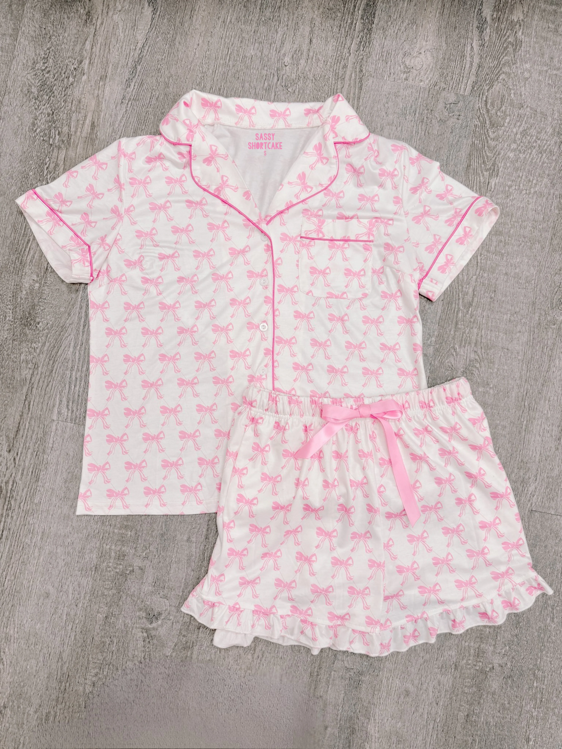 Pink bow print pajama set; short sleeves, shorts with ruffle trim.
