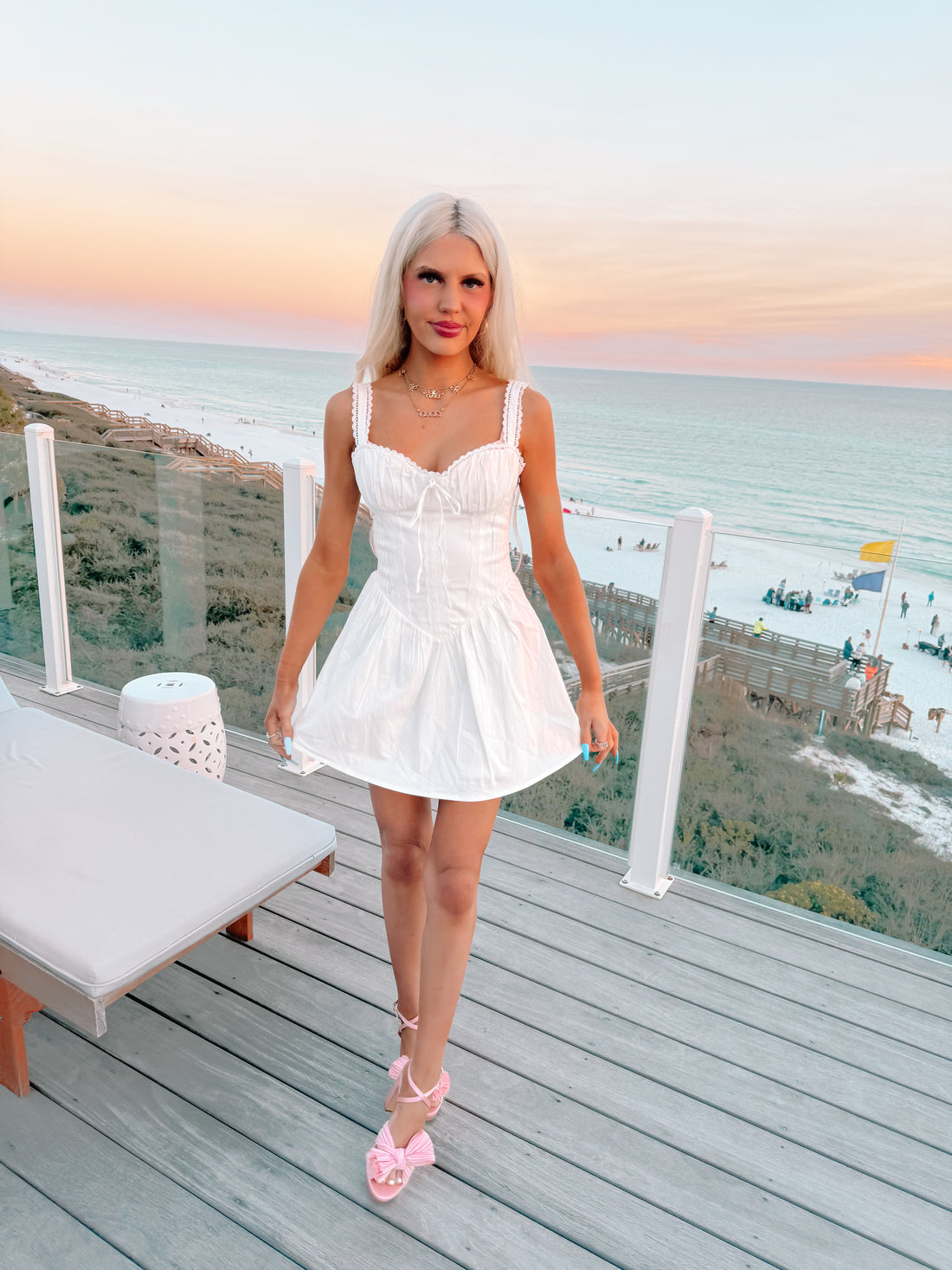White corset mini dress on a beachside deck at sunset.
