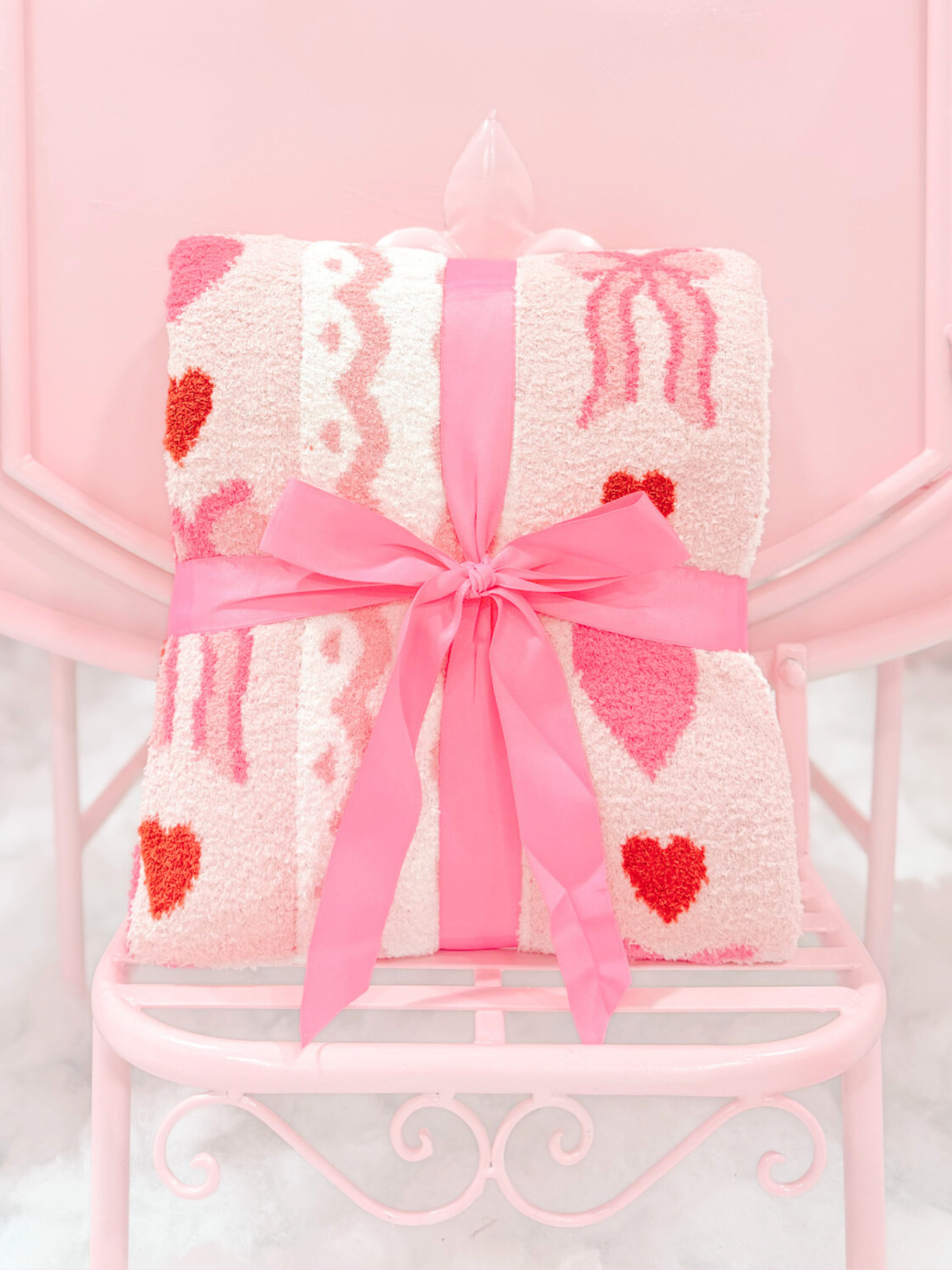 Love Bow Blanket from Sassy Shortcake – folded pink throw blanket with heart pattern tied with a pink satin ribbon on chair