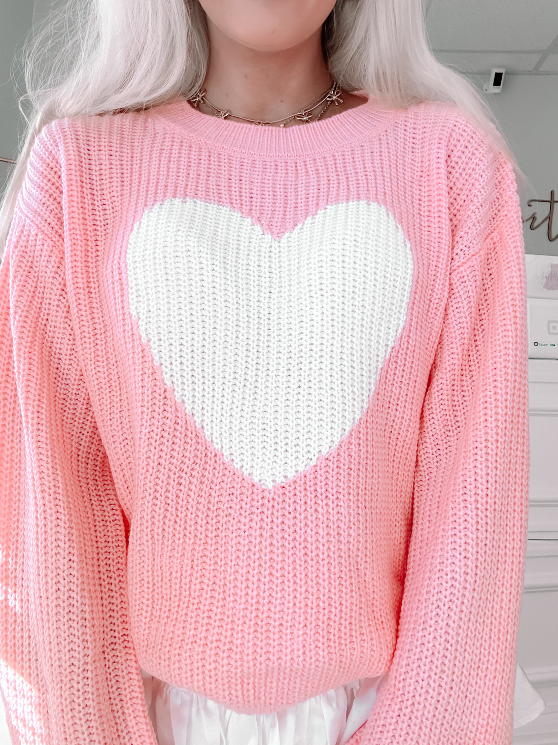 Pink knit sweater featuring a large white heart design.
