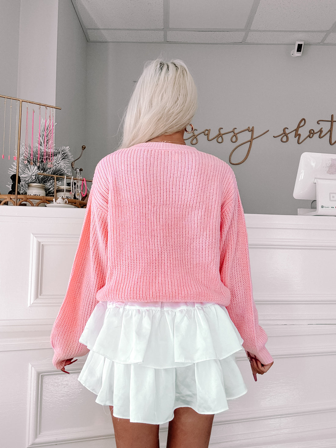Pink knit sweater with balloon sleeves, shown from the back, paired with a white tiered skirt.

