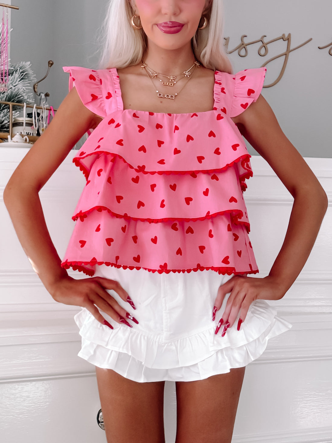 Pink tiered ruffle top adorned with red hearts, styled with white ruffle shorts.
