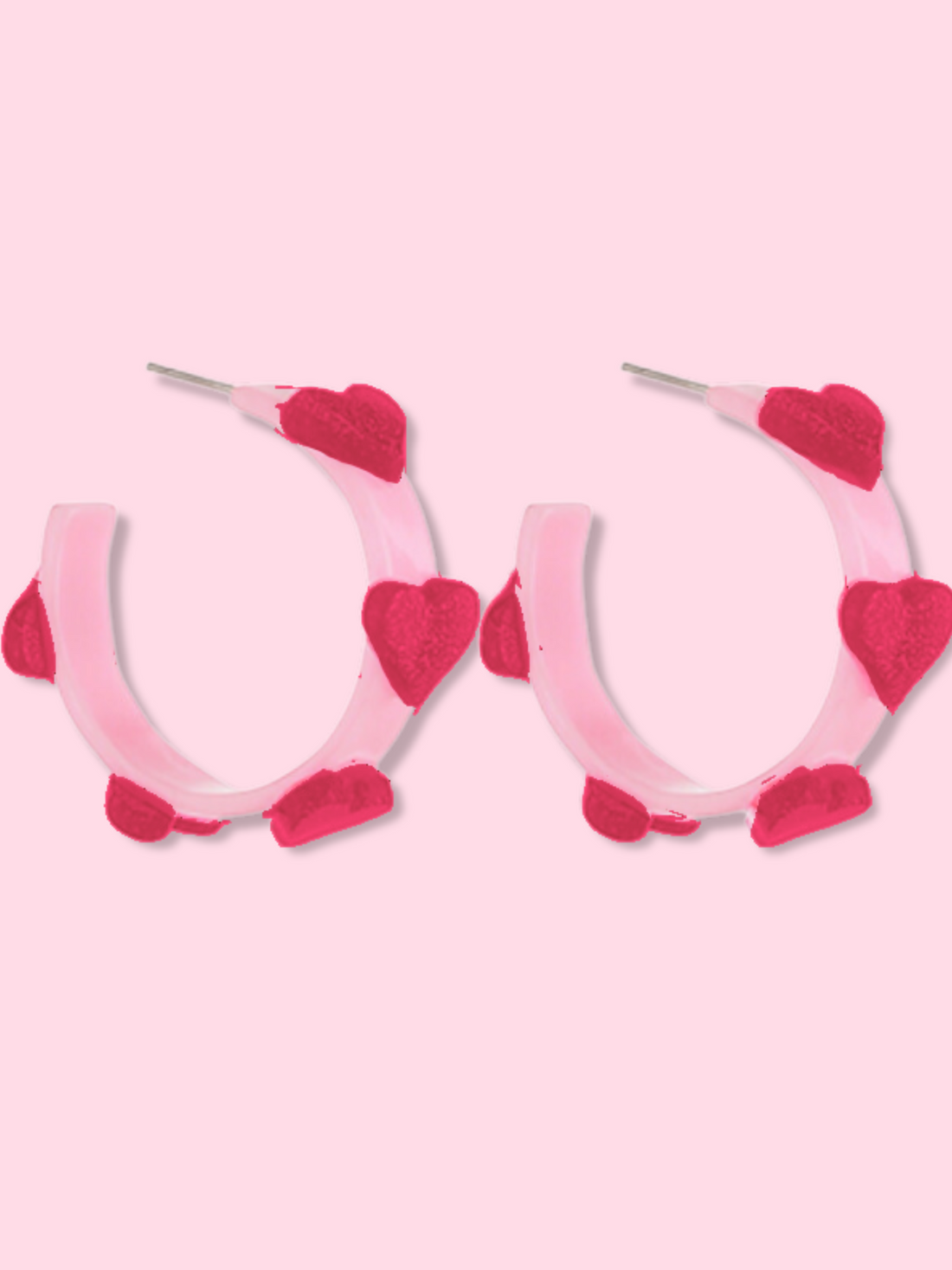 Pink hoop earrings adorned with crimson hearts, shown against a light pink background.

