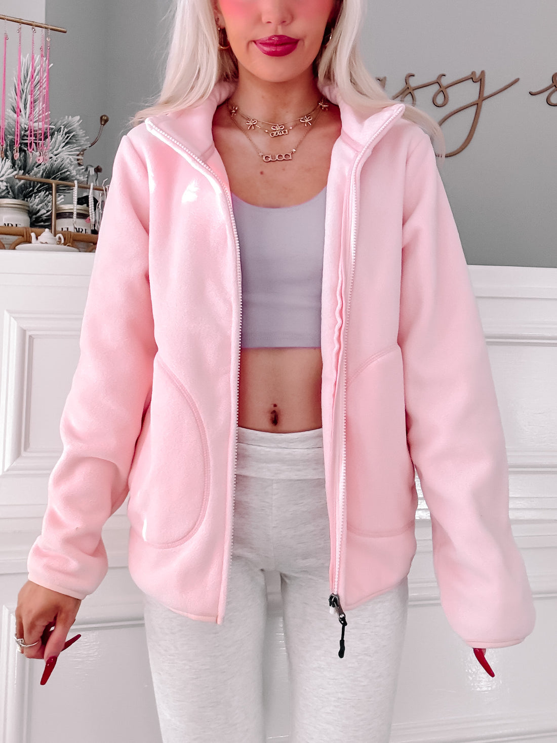 Pink fleece zip-up jacket styled with grey leggings, shown on a model against a white wall.
