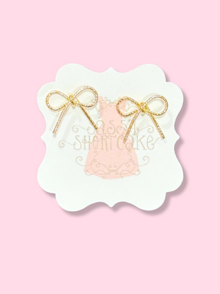 Gold Marlee bow earrings on pink background
