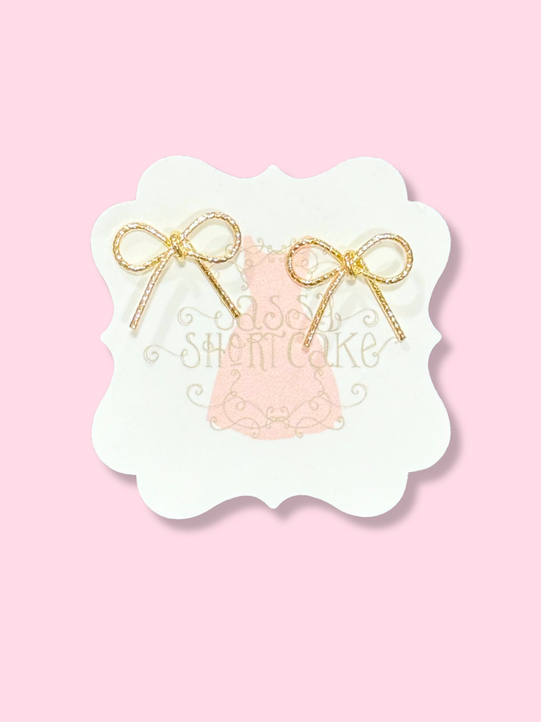 Gold Marlee bow earrings on pink background
