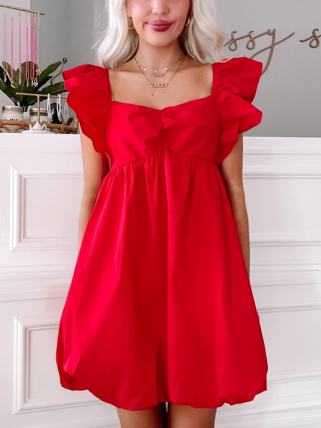 Red bubble mini dress with flutter sleeves, shown on a model against a white wall.
