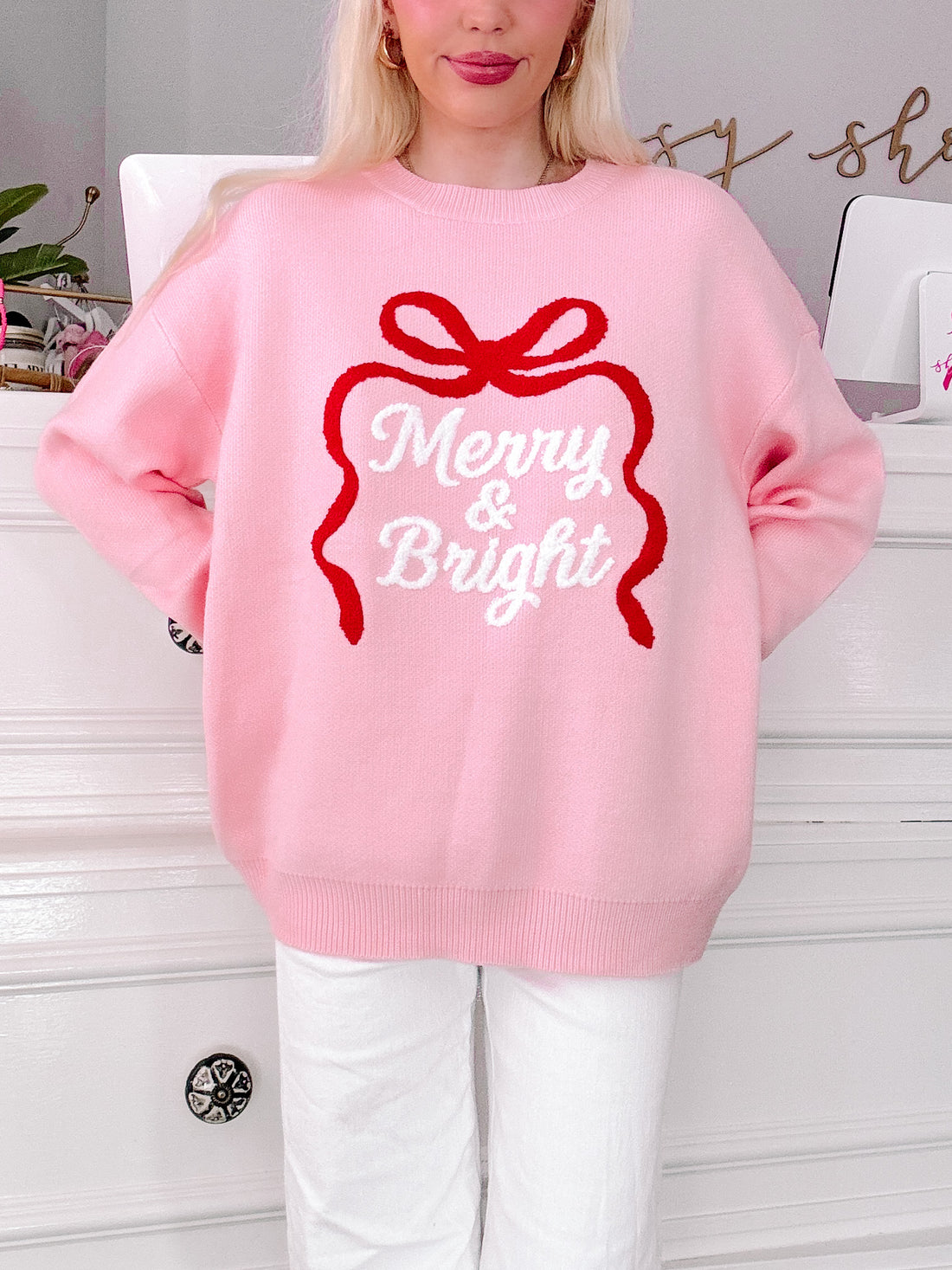 girl wearing a pink sweater with 'Merry & Bright' text and red bow design from sassy shortcake