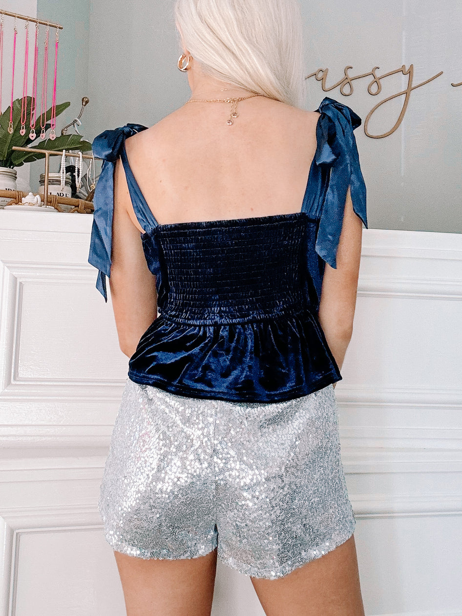 Dark blue velvet top with satin tie straps, paired with silver sequin shorts.
