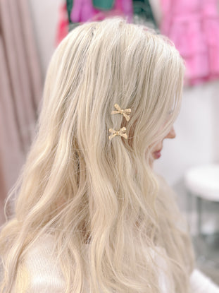 Gold bow hair clips in blonde hair.
