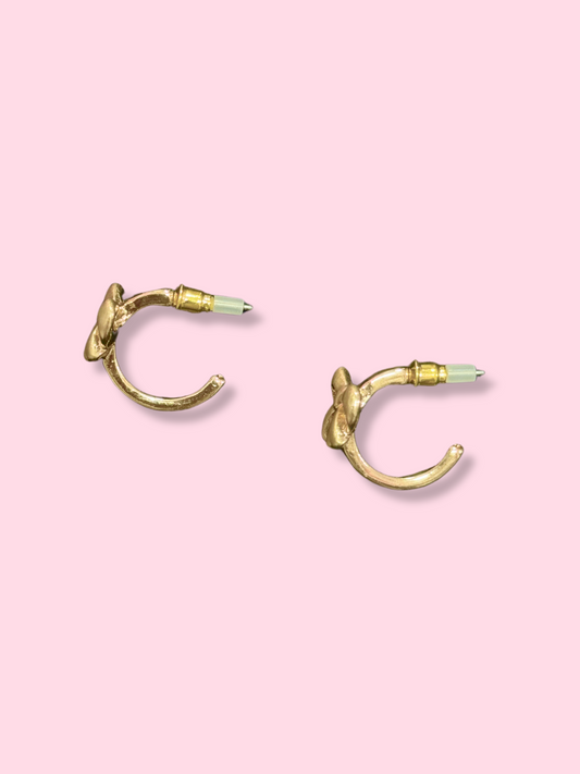 Gold bow-shaped hoop earrings shown on a pink background.