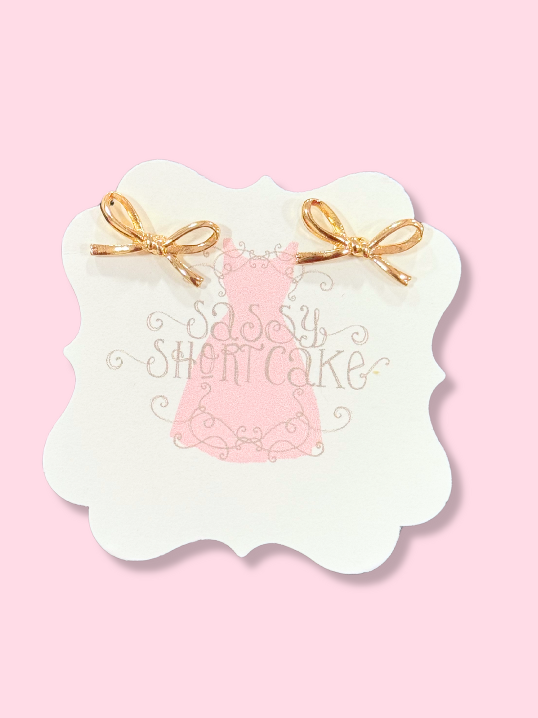 Gold Mini Ties Bow earrings on pink background
