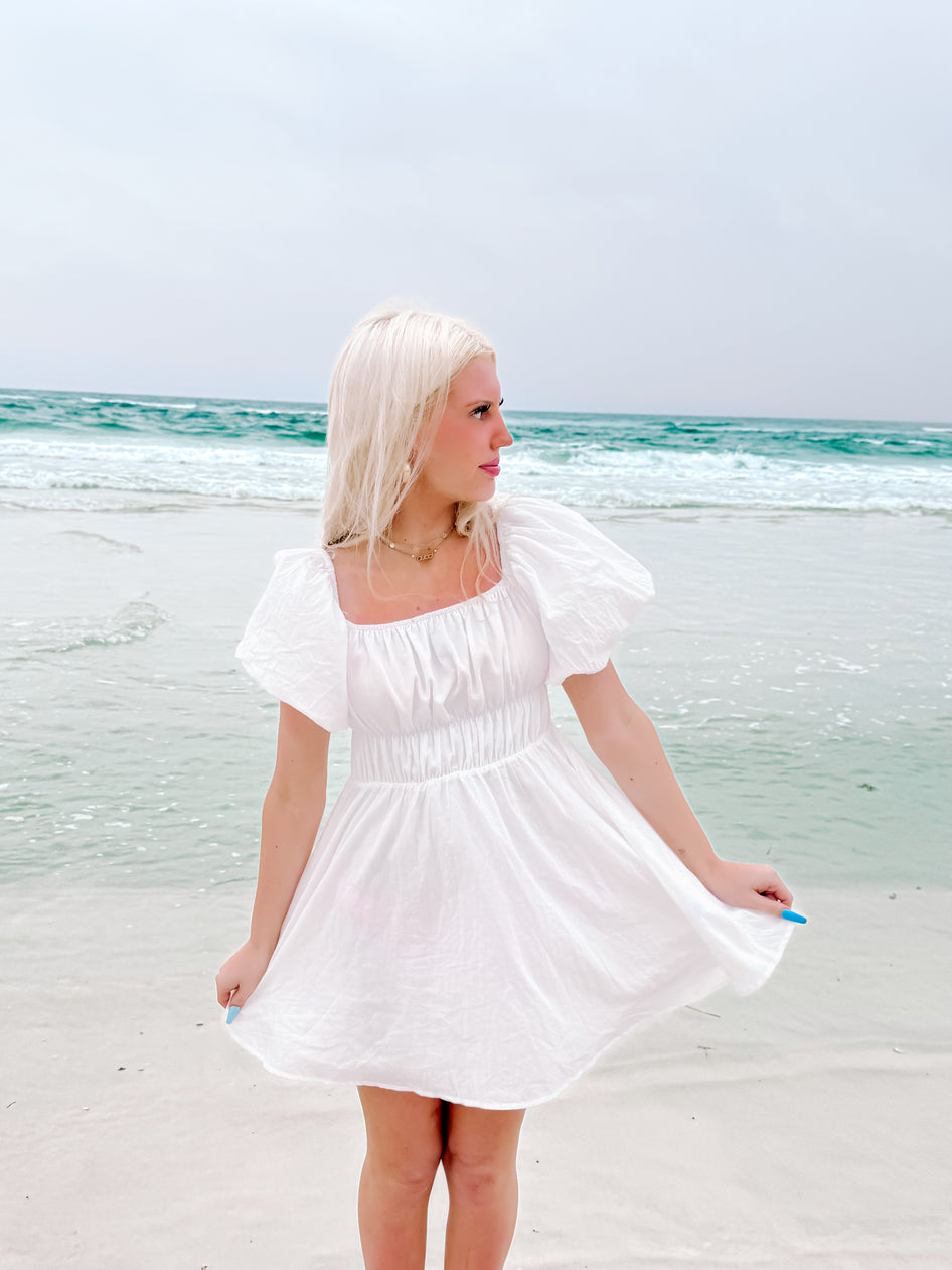 White summer dress on beach, ocean backdrop.
