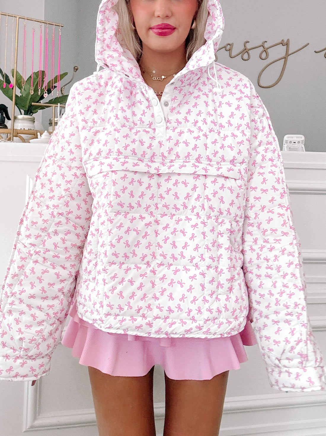 Paige Bow Pullover: White quilted pullover with pink bow print, featuring a hood and button closure.
