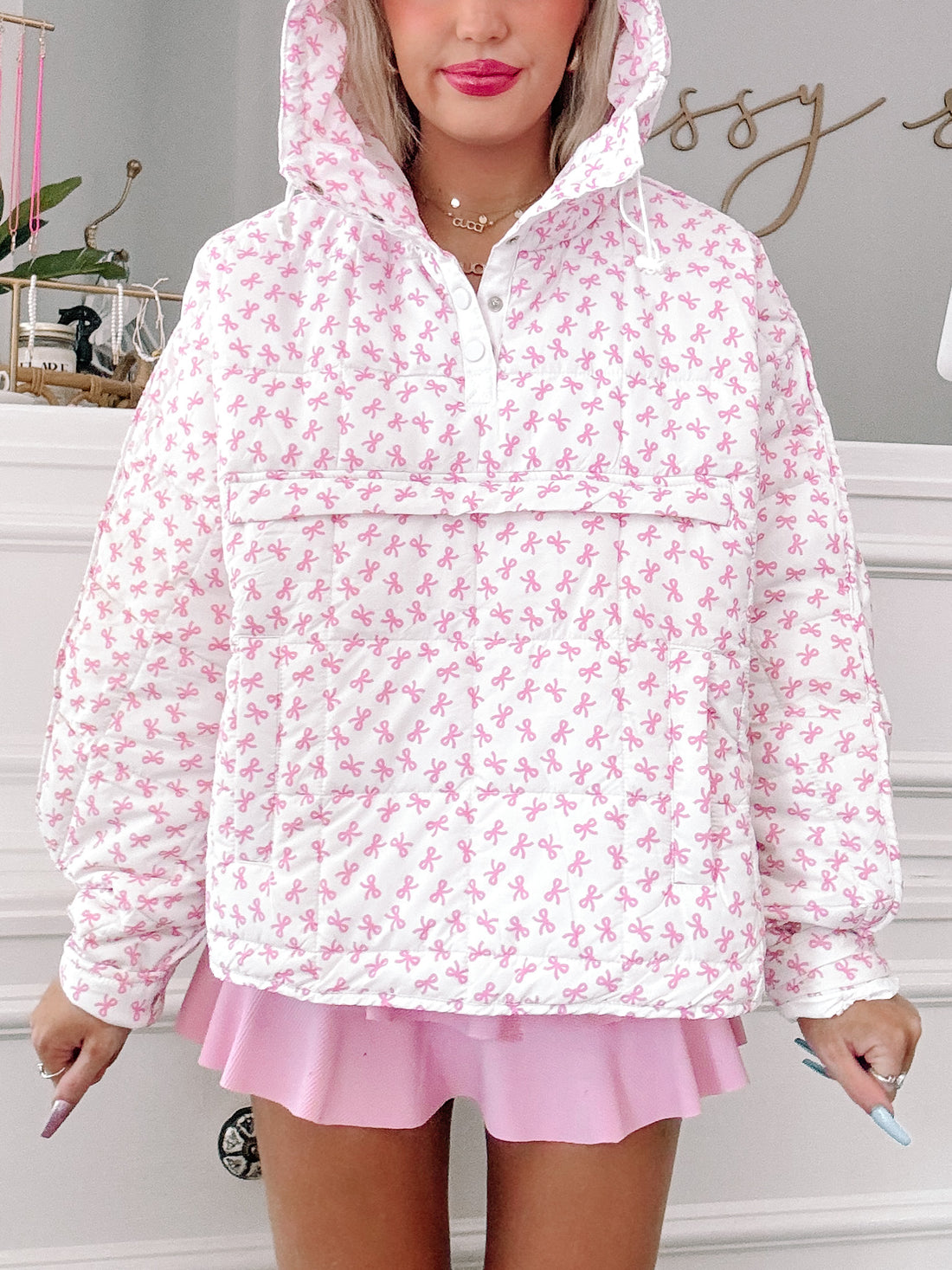 White quilted pullover with pink bow print, featuring a hood and snap closure.
