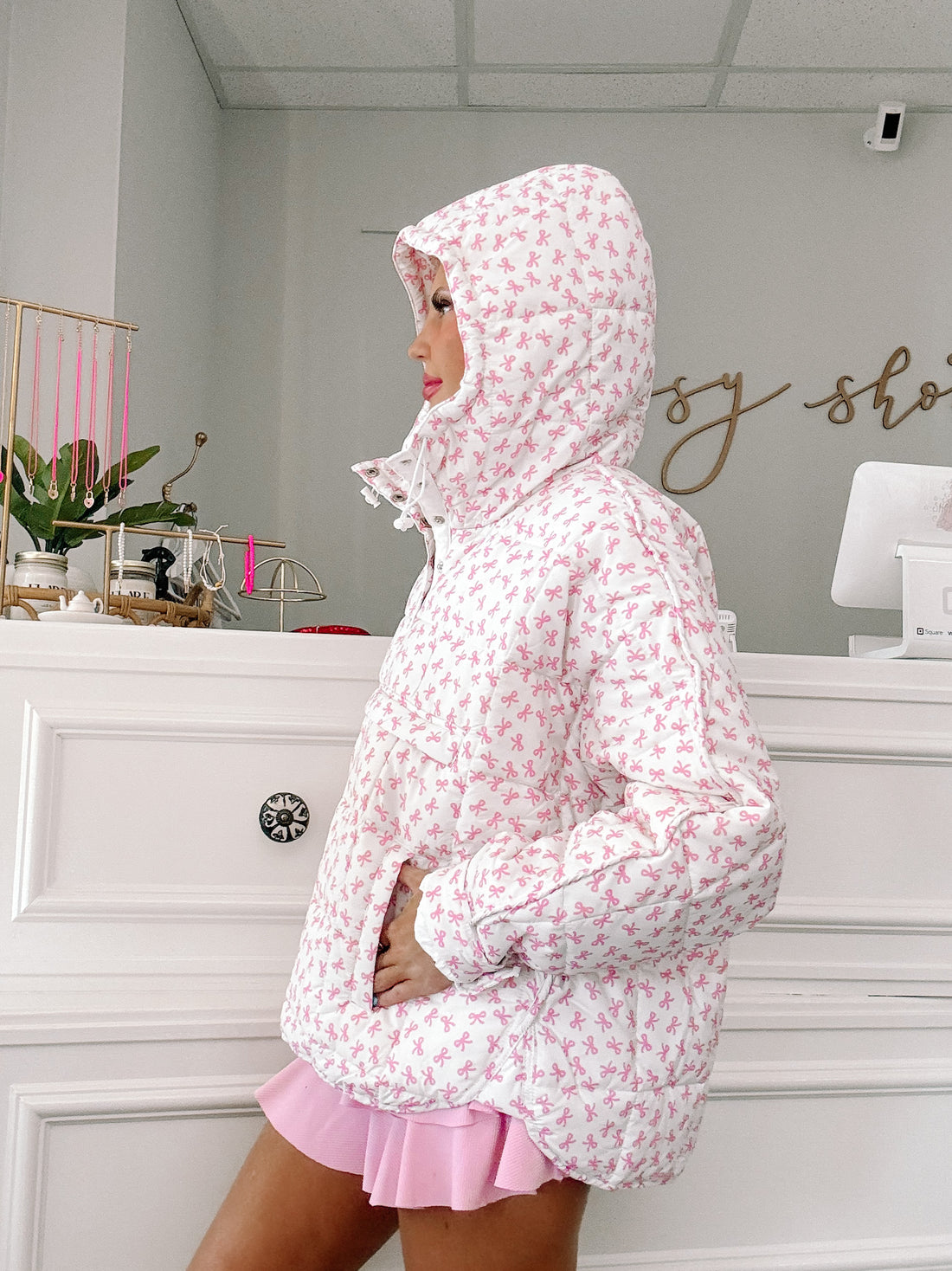 White quilted pullover with pink bow print, modeled in a boutique.
